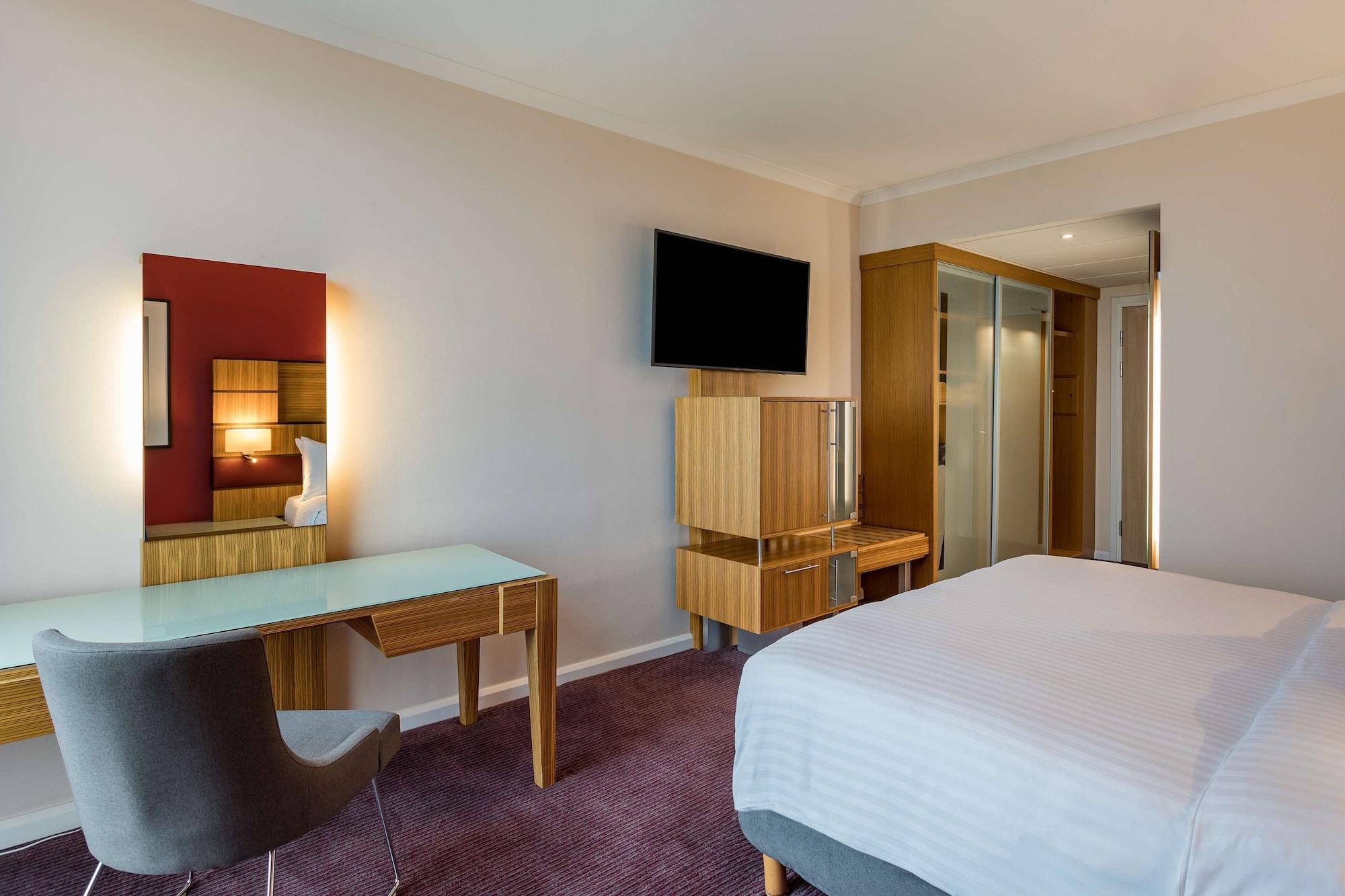 Radisson Blu Hotel London Stansted Airport Stansted Mountfitchet Esterno foto The photo shows a modern hotel room. It features a bed with white bedding, a flat-screen television mounted on the wall, and a contemporary desk with a chair. There is also a mirror on the wall above the desk, and a wooden unit that appears to have s